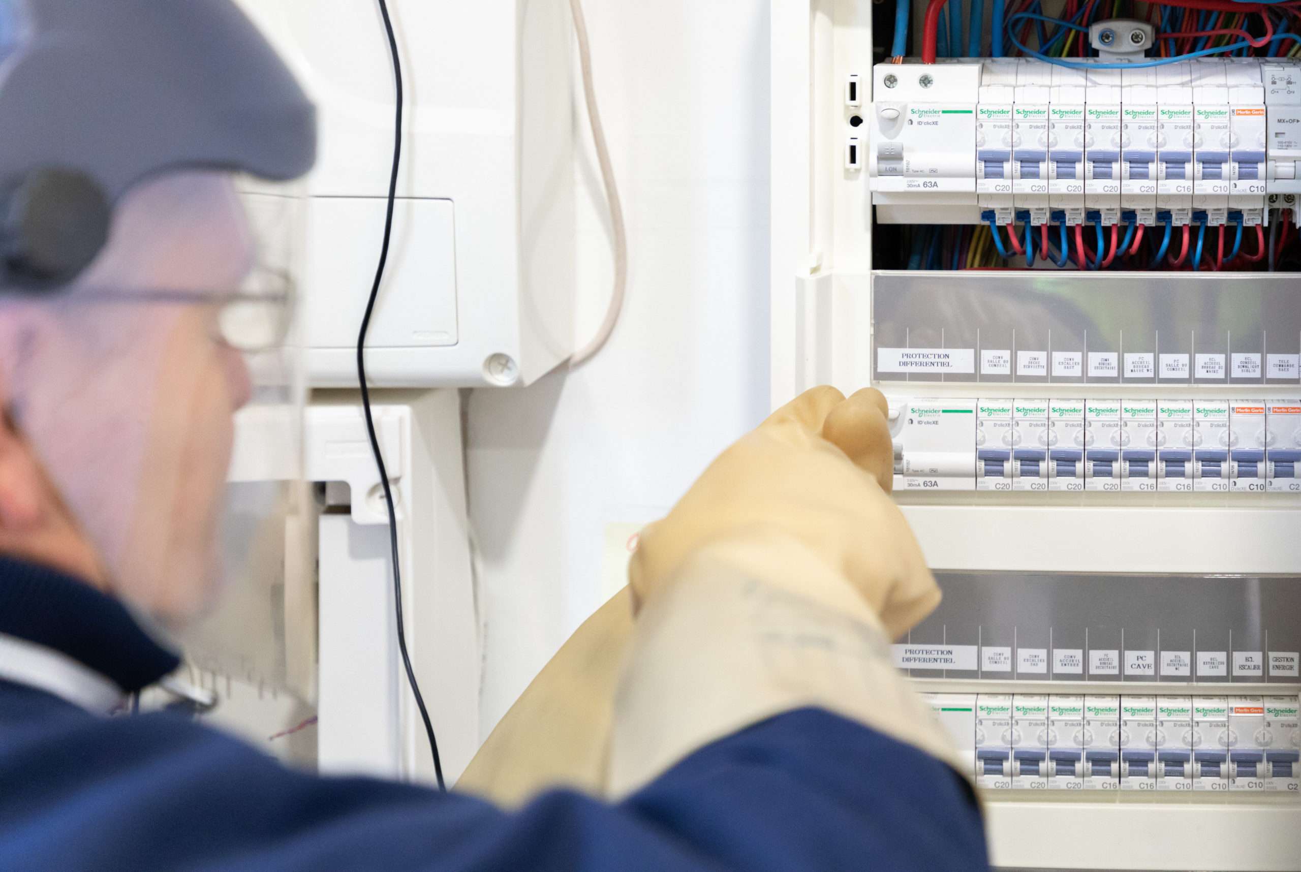 technicien avec EPI (casque) effectuant son contrôle électrique avec des gants de protection